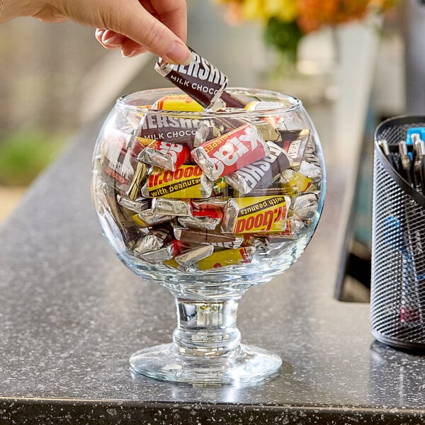 HERSHEY's Assorted Miniature Candy being put into a glass bowl on a hotel buffet counter.