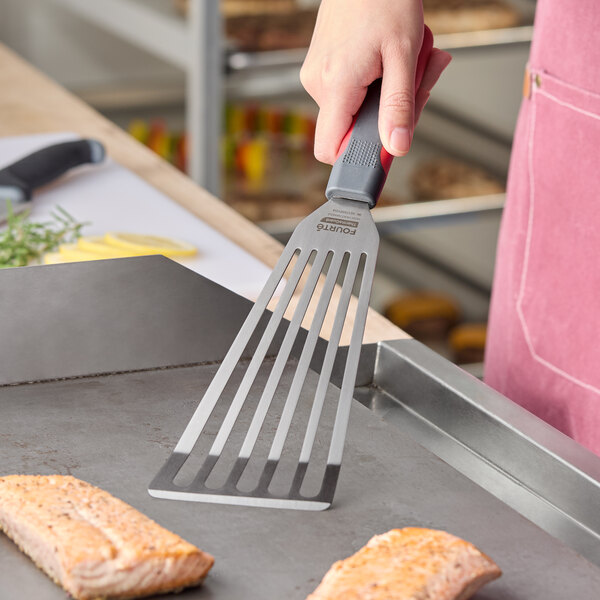 A stainless steel slotted fish and egg turner with a nylon handle being used on a griddle.