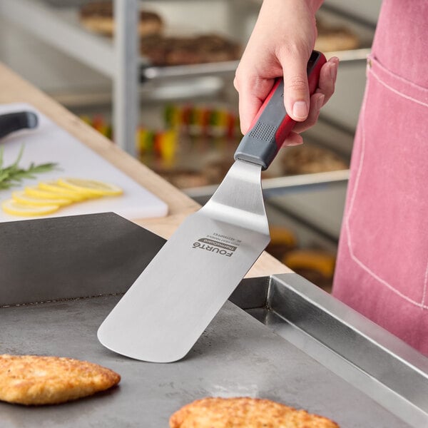A stainless steel high heat solid rounded edge turner with a nylon handle being used on a griddle.