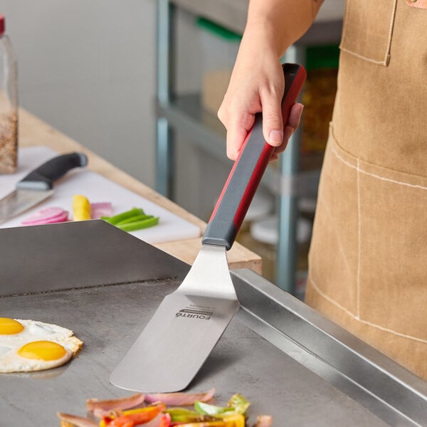 A stainless steel solid rounded edge turner with a long nylon handle being used on a griddle.