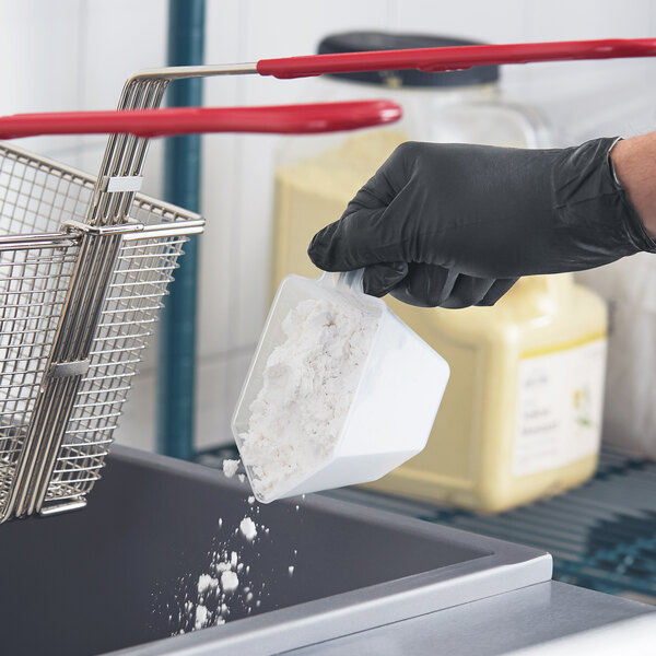 A scoop of white diatomaceous earth fry oil filter powder being poured into a fryer by a person wearing a black glove.