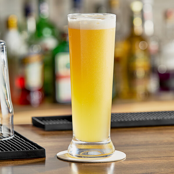 A glass of yellow liquid on a yellow surface with a glass of beer on a coaster.