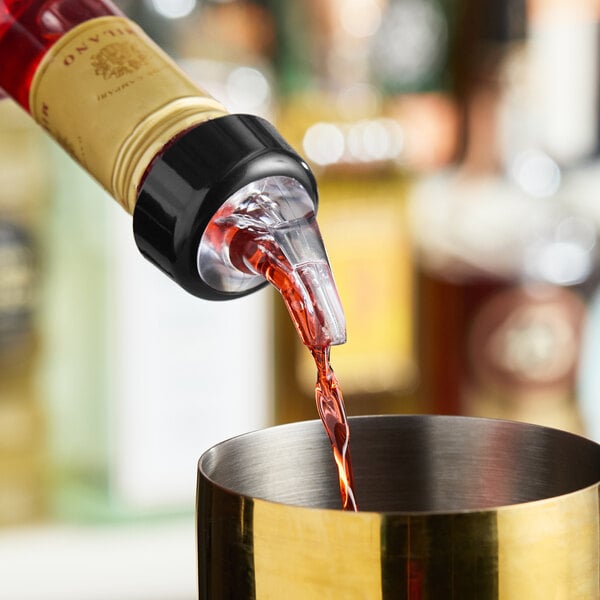 A bottle with a measured liquor pourer dispensing liquid into a metal container.