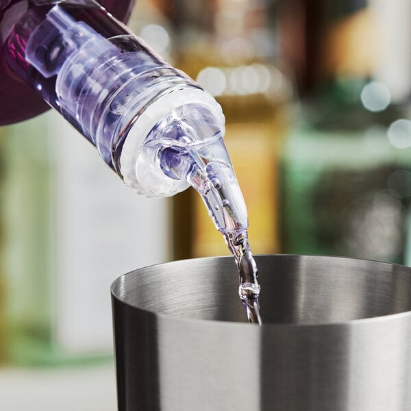 A close-up of a measured liquor pourer dispensing liquid into a stainless steel cup.
