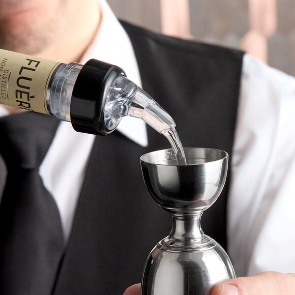 A close-up of a bottle with a measured liquor pourer dispensing liquid into a stainless steel jigger.