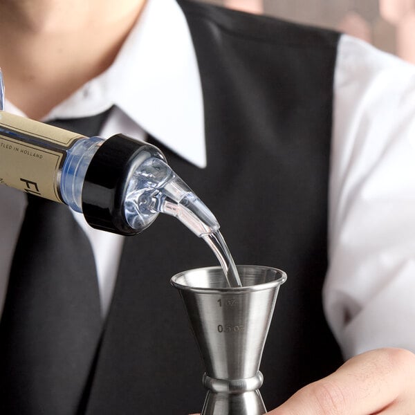 A person pours liquid from a bottle fitted with a measured liquor pourer into a metal jigger.