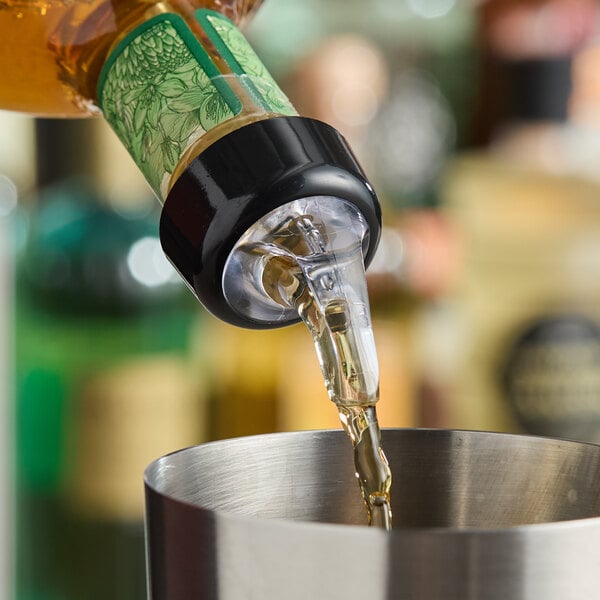 A bottle with an Acopa 1.25 oz. 3-ball measured liquor pourer with collar dispensing liquid into a metal container.