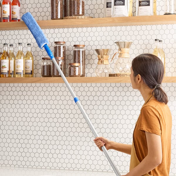 A woman using a Lavex telescoping wand with a duster sleeve to clean shelves.
