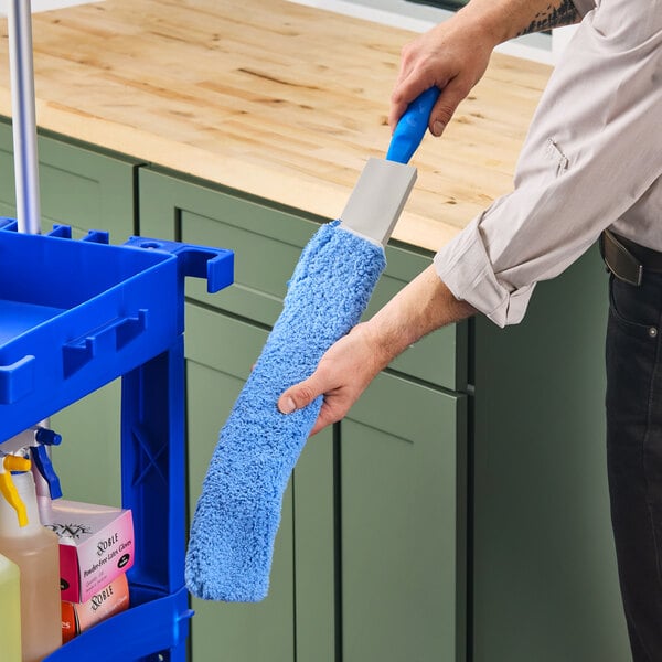 A person holding a blue microfiber sleeve on a cleaning cart.