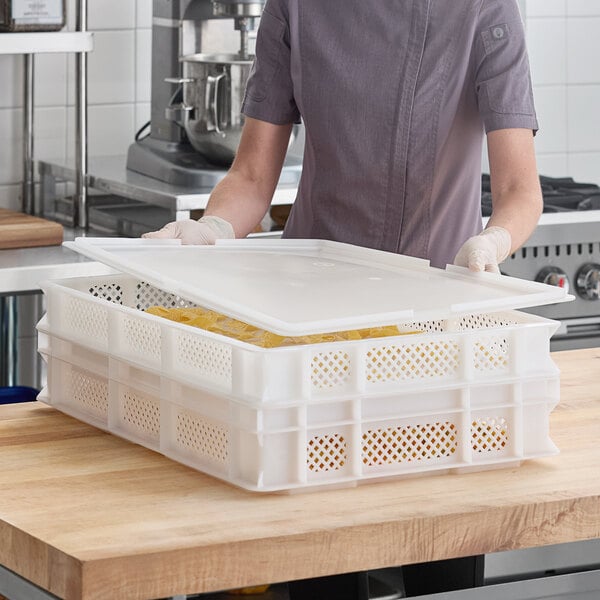 A white perforated plastic pasta drying box with a lid, placed on a wooden countertop in a commercial kitchen.