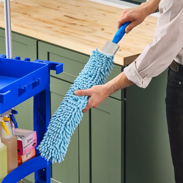 A hand holding a blue Lavex Flex Wand Duster with a chenille sleeve.