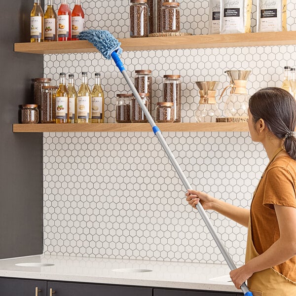 A woman using a Lavex Flex Wand Duster with a chenille sleeve to dust shelves.