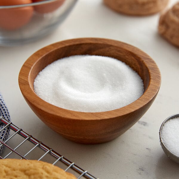 A bowl of sugar next to cookies and a cookie cutter on a counter.