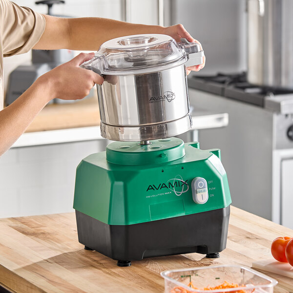 A green and black AvaMix Revolution Max combination food processor with a stainless steel bowl being placed on its base.