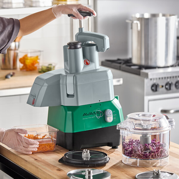 A commercial combination food processor with a clear plastic bowl, continuous feed attachment, and multiple discs for slicing and shredding.