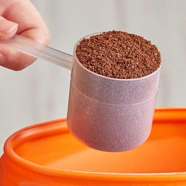 A hand using a 70 cc Polypropylene scoop to fill a container with brown granules.