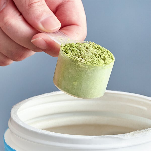 A hand holding a white polypropylene scoop with green powder.