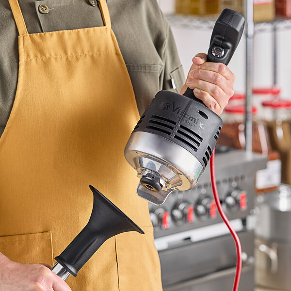 A person using a Vitamix Immersion Blender in a professional kitchen.