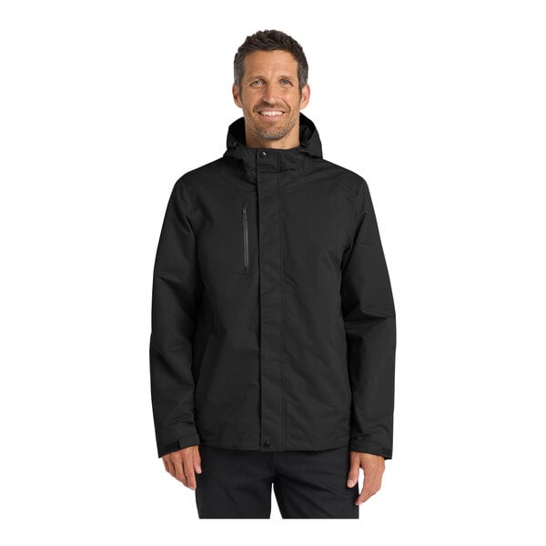 A man wearing a black Port Authority all-conditions parka jacket with a hood.