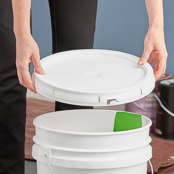 A person's hand placing a white plastic lid on a white bucket.