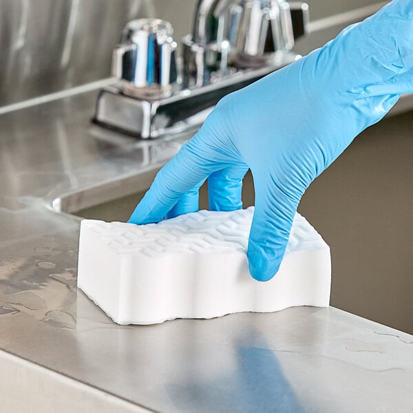 A hand in a blue glove using a white Mr. Clean Magic Eraser on a counter.