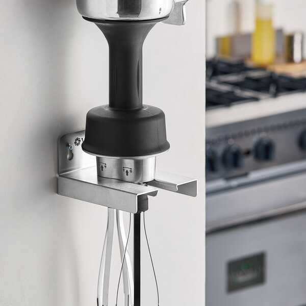 A stainless steel detachable whisk attachment for immersion blenders mounted on a wall bracket.
