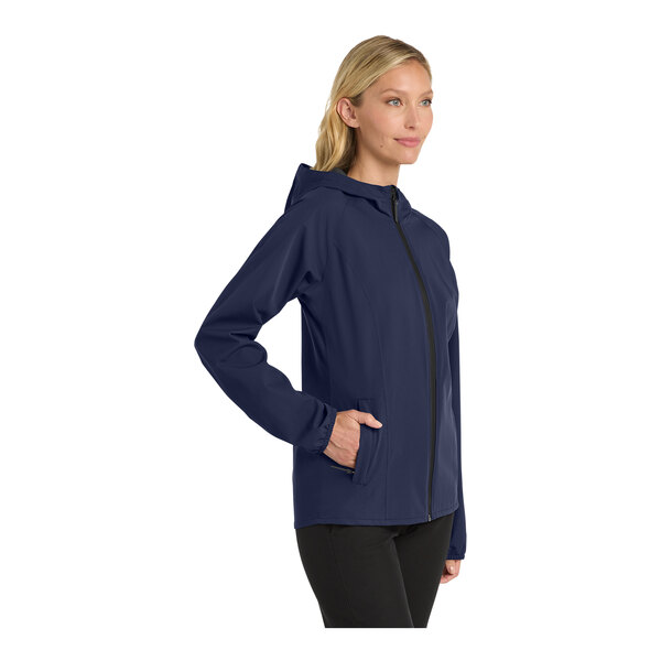 A woman wearing a Port Authority navy rain jacket with a hood and zipper.
