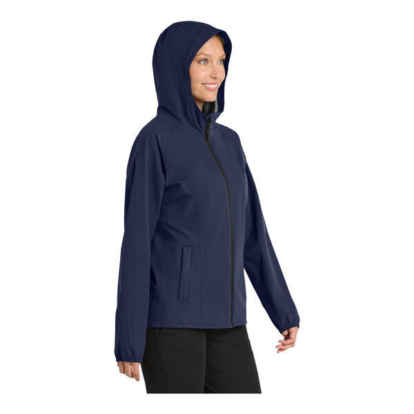 A woman wearing a navy Port Authority rain jacket with a hood and zipper.