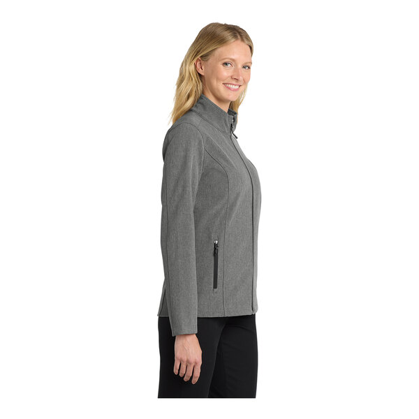 A woman wearing a Port Authority pearl gray heather soft shell jacket.