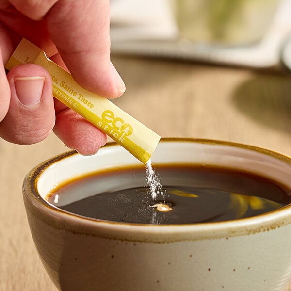 A hand holding an ecoStick Yellow Sucralose packet over a cup of coffee.