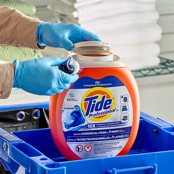 A person in blue gloves putting Tide Professional laundry detergent pods in a blue container.