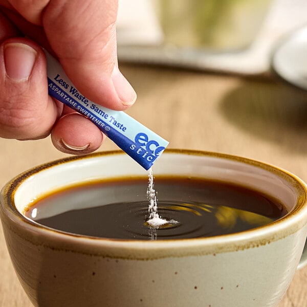 A hand holding an ecoStick Blue packet of powder over a cup of coffee.