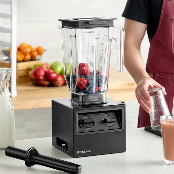 A person pouring fruit into a Blendtec commercial blender on a counter.