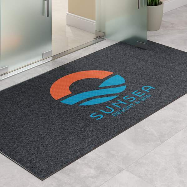 A large rectangular dark gray entrance mat with a colorful logo and text, designed for indoor or outdoor use.