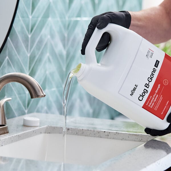 A gallon container of Noble Clog-B-Gone Ultra industrial pro-strength drain opener being poured into a sink.