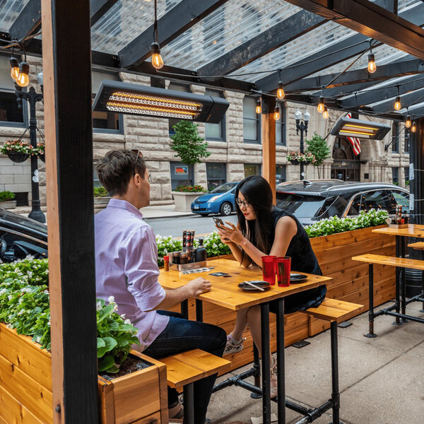A man and woman sitting at a table on an outdoor patio with a GHOST INFRARED BLACK ALUM patio heater on the table.
