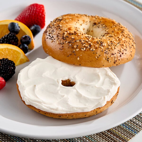 A plain bagel with John F. Martin whipped cream cheese and fruit on a plate.