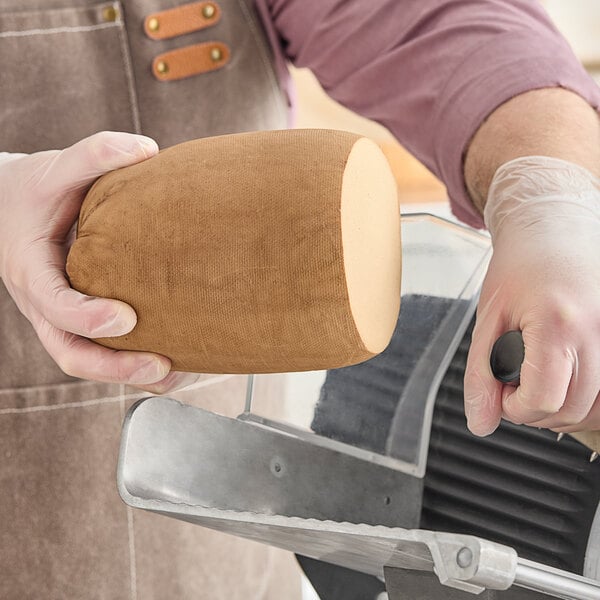 A man using a knife to cut Prime Roots Vegan Classic Smoked Koji-Turkey deli meat on a counter.