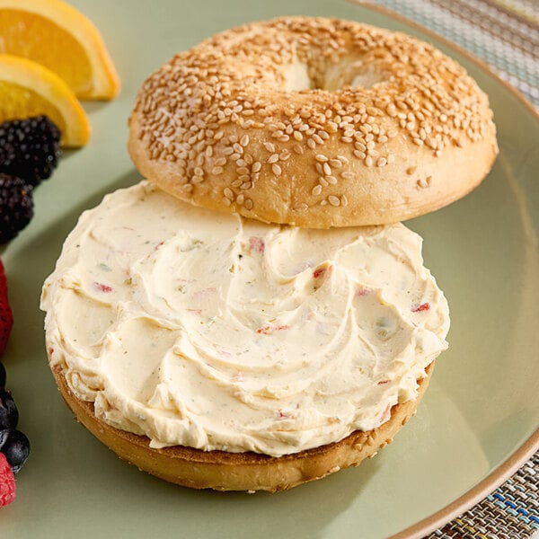 A bagel with John F. Martin vegetable cream cheese and fruit on a plate.