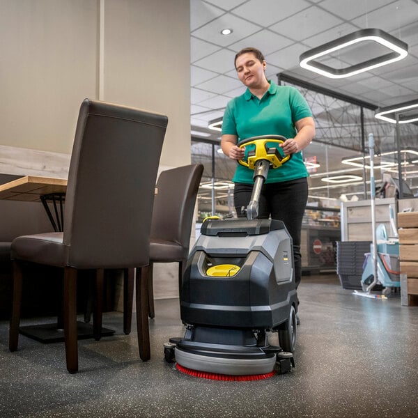 A person operating a Karcher BD 35/15 C BP Classic 14-inch cordless walk-behind floor scrubber in a commercial setting.
