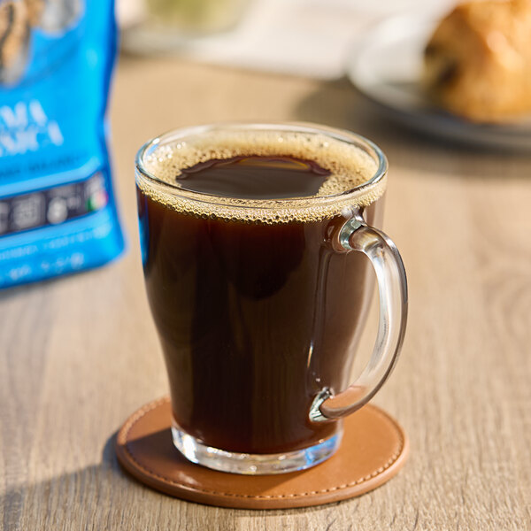A glass mug of Caffe Borbone coffee on a coaster next to a bag of Caffe Borbone whole bean espresso.
