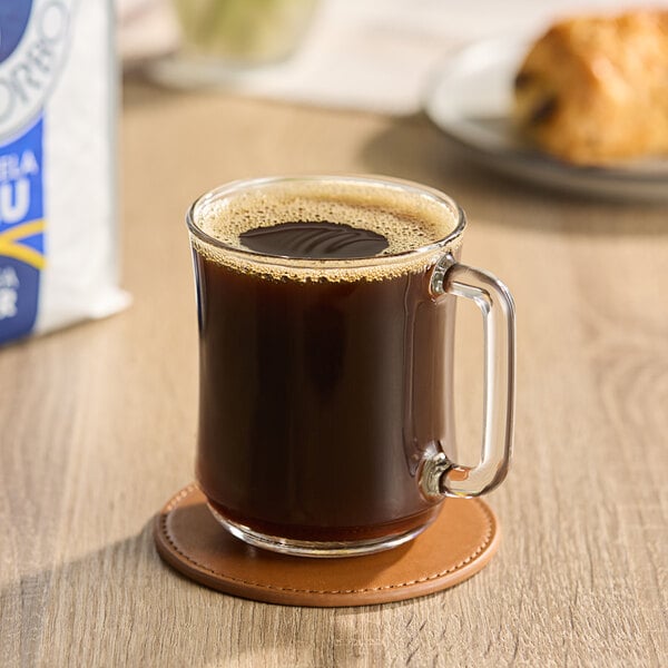 A glass mug of Caffe Borbone Blue Blend espresso on a coaster on a table.