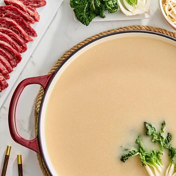 A large pot of tonkotsu ramen soup with leafy greens and meat.
