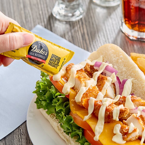 A person putting a Duke's Real Mayonnaise packet on a chicken sandwich.