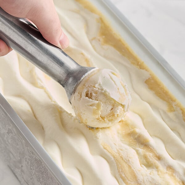 A person scooping Villa Dolce Torta Al Limone (Lemon Pie) Gelato into a pan with a metal scoop.
