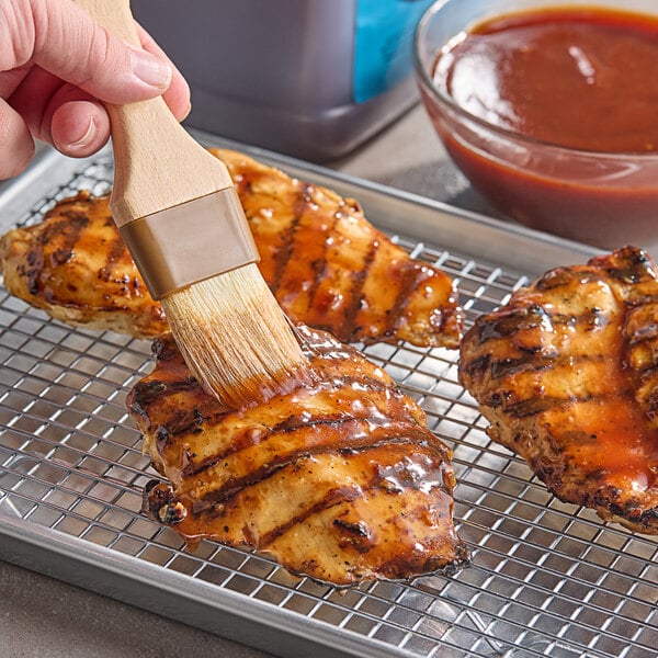 A person brushing Duke's Sweet BBQ Sauce on chicken breasts.