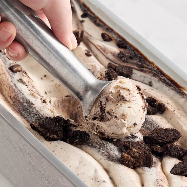 A person scooping Villa Dolce Traditional Cookies & Cream Gelato into a metal pan.