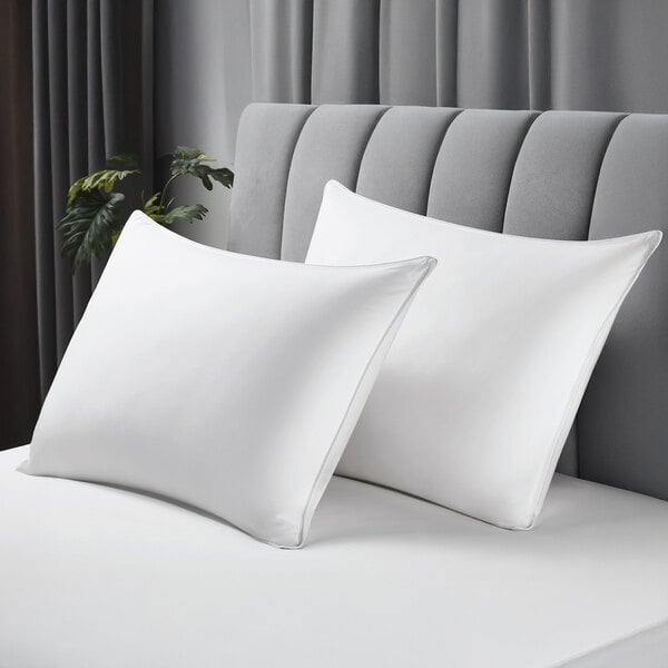 A pair of white king size pillows with cotton covers on a bed with a gray upholstered headboard.