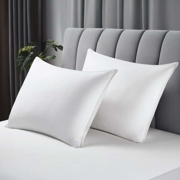 A pair of standard size white pillows with cotton covers on a bed.