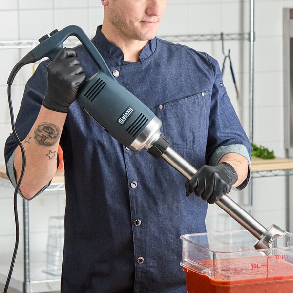 A heavy-duty Galaxy IMBH16 16-inch variable speed immersion blender being used to blend ingredients in a large container.